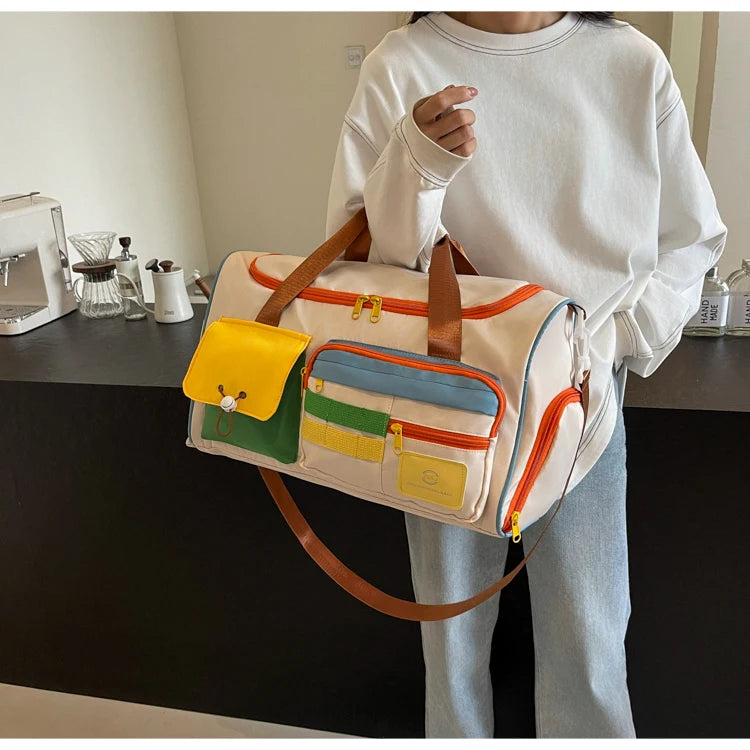 Woman in a white sweatshirt holding a colorful nylon duffel bag with multiple front pockets and orange zippers, styled for casual travel or gym use
